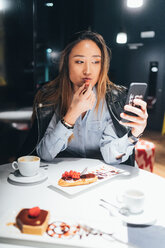 Woman sitting in restaurant, eating dessert, using smartphone - CUF45213