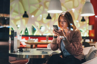Woman sitting in restaurant, using smartphone - CUF45214