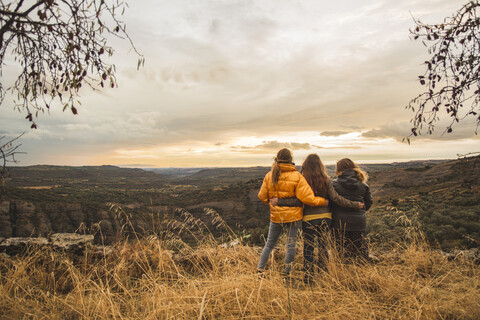 Spanien, Alquezar, drei Freunde umarmen sich auf einem Hügel mit Blick auf die Landschaft, lizenzfreies Stockfoto