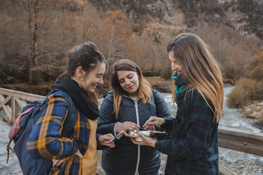 Spanien, drei junge Frauen beim Betrachten von Sofortbildern auf einer Brücke im Ordesa-Nationalpark - AFVF01638