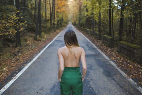 Rückansicht einer jungen Frau ohne Hemd, die auf einer Landstraße steht, lizenzfreies Stockfoto
