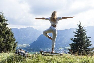 Deutschland, Bayern, Oberammergau, junge Frau macht Yoga auf Bank auf Bergwiese - TCF05842