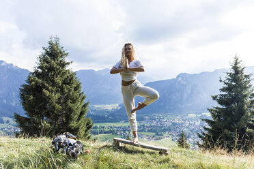 Deutschland, Bayern, Oberammergau, junge Frau macht Yoga auf Bank auf Bergwiese - TCF05844
