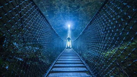 Mysteriöse silhouettierte Person auf Hängebrücke im Wald bei Nacht - FSIF03199