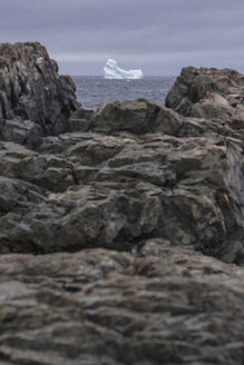 Blick auf einen Eisberg im Meer durch Felsen am Ufer, Fogo Island, Neufundland, Kanada - FSIF03200