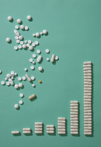 Pillen verstreut über Kapseln, die ein aufsteigendes Balkendiagramm auf grünem Hintergrund bilden, lizenzfreies Stockfoto