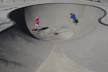 Bruder und Schwester auf Motorrollern spielen im sonnigen Skatepark - FSIF03224