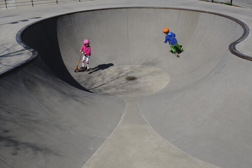 Brother and sister on scooters playing at sunny skate park - FSIF03224