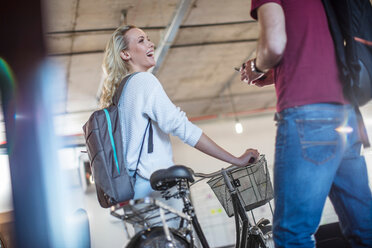 Young woman with bicycle greeting colleague in office - CUF45521