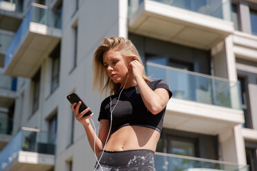Young woman listening to music on mobile phone, building in background - CUF45653