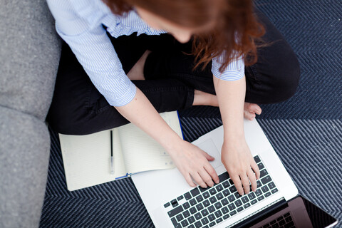 Frau sitzt auf dem Boden und benutzt einen Laptop, lizenzfreies Stockfoto