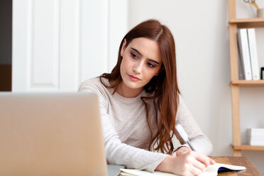 Woman writing notes into notepad from laptop - CUF45699