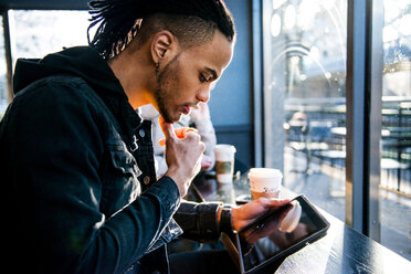 Junger Mann sitzt in einem Café und schaut auf ein digitales Tablet, London, England, UK - CUF45726