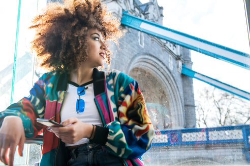 Junge Frau im Freien, hält Smartphone, schaut weg, Tower Bridge im Hintergrund, London, England, UK - CUF45728