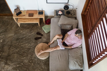 Mature man on sofa reading book, overhead view - CUF45743