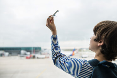 Boy playing with toy airplane in airport departure lounge - CUF45762