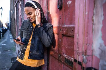 Man in street listening to music through headphones on smartphone - CUF45788