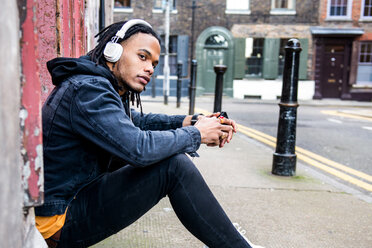 Man sitting in street listening to music through headphones - CUF45789