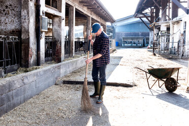 Dairy farm worker sweeping farm yard - CUF45827