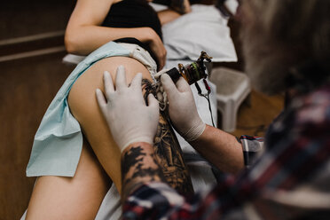 Tattooist tattooing young woman's thigh, close-up - CUF45862