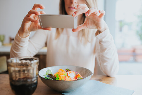 Frau fotografiert vegane Mahlzeit im Restaurant, lizenzfreies Stockfoto