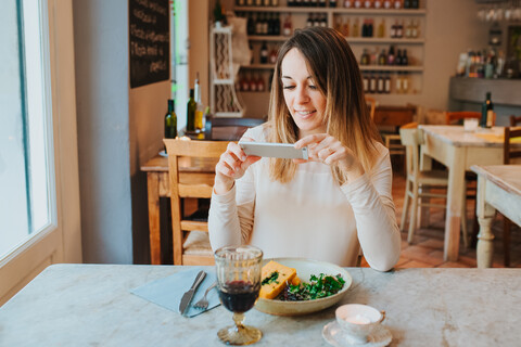 Frau fotografiert vegane Mahlzeit im Restaurant, lizenzfreies Stockfoto