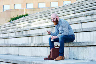 Bärtiger Mann sitzt auf einer Stufe und benutzt ein Smartphone - CUF45942