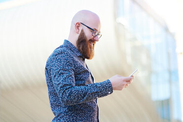 Bearded man texting on smartphone, smiling - CUF45950