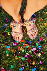 Overhead view of young woman standing amongst confetti on grass at Holi Festival, detail of feet - CUF45958