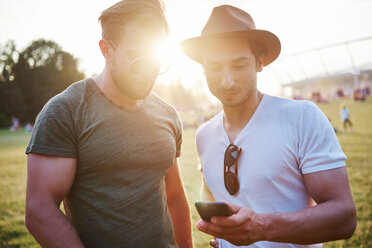 Zwei junge Männer schauen beim Holi-Festival auf ihr Smartphone, Detail der Füße - CUF45959