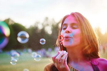 Young woman covered in coloured chalk powder blowing bubbles at Holi Festival - CUF45964