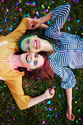 Two young women covered in coloured chalk powder lying on grass at Holi Festival, overhead portrait - CUF45976