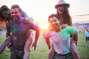 Two young couples covered in coloured chalk powder piggybacking at Holi Festival - CUF45983