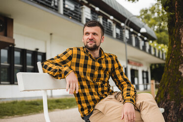 Mann sitzt auf einer Parkbank vor einem Hotel, Dolenci, Slowenien - CUF45991