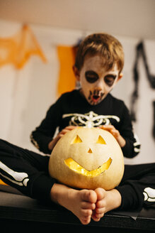 Kleiner Junge mit bemaltem Gesicht und Kostüm sitzt barfuß auf einem Tisch mit Jack O'Lantern - JRFF01883