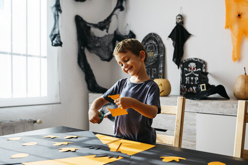 Smiling little boy cutting out for Halloween decoration at home - JRFF01886