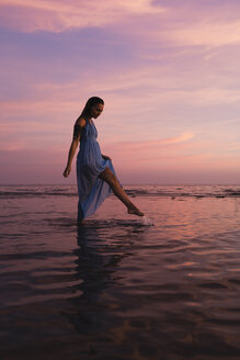 Junge Frau mit Tattoo steht vor dem Meer bei Sonnenuntergang - MAUF01727