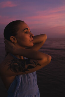 Profil einer jungen Frau mit Tattoo vor dem Meer bei Sonnenuntergang - MAUF01729