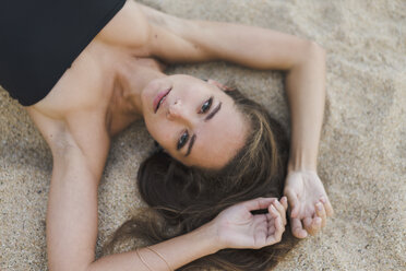 Overhead portrait of beautiful young woman lying in sand - AFVF01743