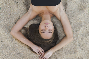 Overhead view of beautiful young woman lying in sand with closed eyes - AFVF01744