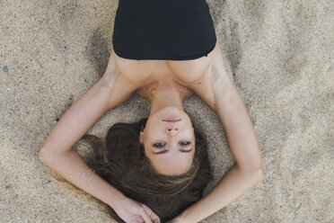 Overhead portrait of beautiful young woman lying in sand - AFVF01745