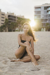 Porträt einer schönen jungen Frau, die bei Sonnenuntergang am Strand sitzt - AFVF01747