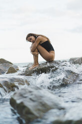 Beautiful young woman wearing swimsuit sitting on rock in the sea - AFVF01751