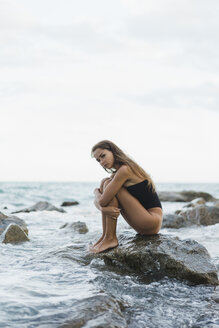 Schöne junge Frau im Badeanzug sitzt auf einem Felsen im Meer - AFVF01752