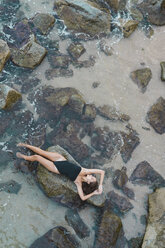 Blick von oben auf eine schöne junge Frau, die auf einem Felsen im Meer liegt - AFVF01754