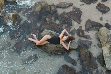 Blick von oben auf eine schöne junge Frau, die auf einem Felsen im Meer liegt - AFVF01755