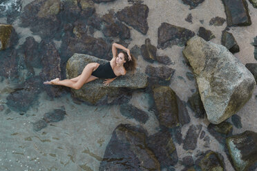 Blick von oben auf eine schöne junge Frau, die auf einem Felsen im Meer liegt - AFVF01756