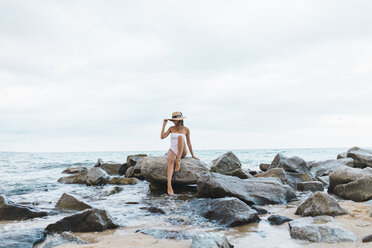 Junge Frau in Badeanzug und Hut sitzt auf einem Felsen im Meer - AFVF01758