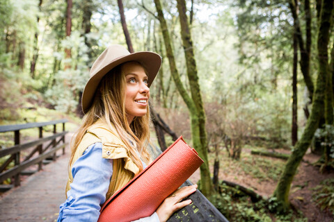 Junge Frau mit Dreispitz schaut von einem Waldsteg auf, lizenzfreies Stockfoto