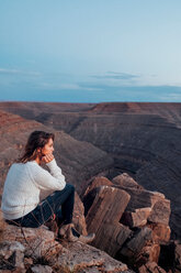 Junge Frau in abgelegener Umgebung, auf Felsen sitzend, mit Blick auf die Aussicht, Mexican Hat, Utah, USA - ISF19757